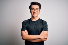 Young Handsome Chinese Man Wearing Black T-shirt And Glasses Over White Background Happy Face Smiling With Crossed Arms Looking At The Camera. Positive Person.