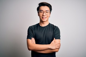 Young handsome chinese man wearing black t-shirt and glasses over white background happy face smiling with crossed arms looking at the camera. Positive person.