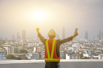 Engineers proudly raise their hands on the job site against the sunrise with the city background.