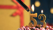 Birthday cake number 53 golden candles burning by lighter, background gift yellow box tied up with red ribbon. Close-up