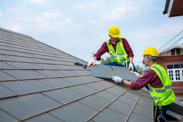 Two construction workers helped to Fixing roof tiles, turning the gray in the house with the blue sky in the safety suit for safety.