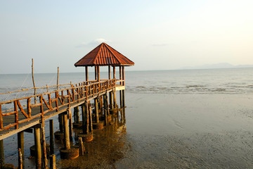 old bridge to building red roof on black sand beach at thailand