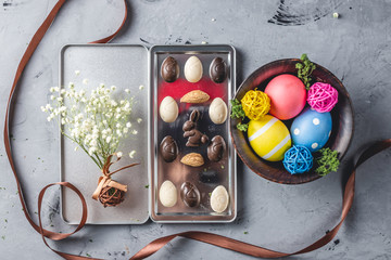 Gift set of chocolate in the shape of eggs and a rabbit in a box with a bouquet of spring flowers and bright Easter eggs