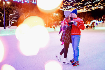 Loving couple drinks hot tea or coffee from thermos mugs on winter street in ice rink night illumination