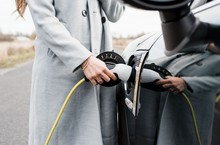 View Of Woman's Hand Plugging In Charging Lead To Her Electric Car