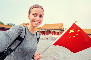 Wall Mural - Enjoying vacation in China. Travel and technology. Young woman with national chinese flag taking selfie in Forbidden City.