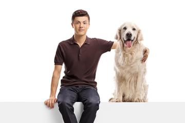 Wall Mural - Young guy sitting on a panel and hugging a retriever dog