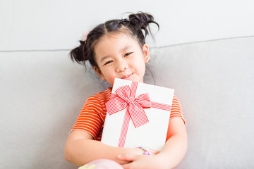 Little asian girl smile and excited and holding red gift box on sofa in living room background.child holding gift box in Christmas and New year concept.