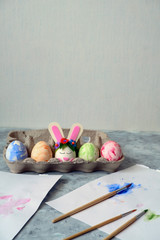 Wall Mural - painted eggs and one egg decorated with bunny ears and paintbrushes on a table against white wall with place for text, diy easter eggs concept