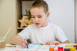 © nadezhda - A boy in a white T-shirt sits at a white table and draws with pencils and paints.