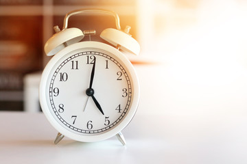 The white clock tells the morning at 5:00 am or evening 17.00 pm, resting on the white table in the room.