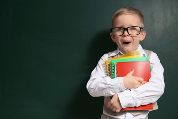 Cute little child wearing glasses near chalkboard, space for text. First time at school