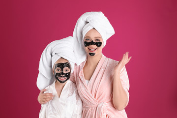 Wall Mural - Happy mother and daughter with black facial masks on pink background