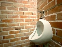 Urinal For Men Are Made Of White Ceramic, Round Shape No Sharp Edge, High Altitude Setup For Adult In The Corner Of The Toilet Or Rest Room As Orange Brick Wall And A Loft Cement, Vintage Or Old Style