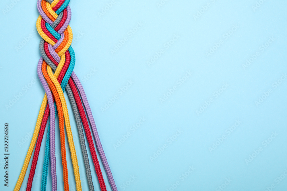 Top view of braided colorful ropes on light blue background, space for text. Unity concept - obrazy, fototapety, plakaty 