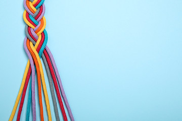 Wall Mural - Top view of braided colorful ropes on light blue background, space for text. Unity concept