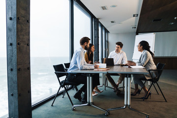 Wall Mural - Image of young female and male colleagues working on laptops in office