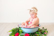 Little cute baby girl is sitting in a basin with pink petals and strawberries.