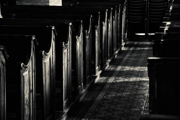 Temple mystery. Wooden benches in dark empty church. Sunlight lightens the pews and passage floor with beautiful pattern. Religious background. Divine light, grace, hope concept. Black white photo.