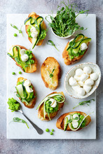 Appetizer Crostini With Mashed Green Pea, Mozzarella, Pea Sprouts And Zucchini Ribbons On White Marble Board. Delicious Healthy Snack, Spring Appetizers