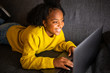 © mimagephotos - happy young african american woman relaxing on sofa looking at laptop computer screen