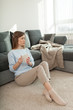 © LifestyleFootage - Young woman holds in her hands cup of tea, sitting on the carpet, relaxing at the day in living room, looking at window