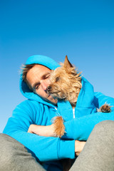 Man sitting with dog in matching blue hooded sweatshirts under bright blue sky