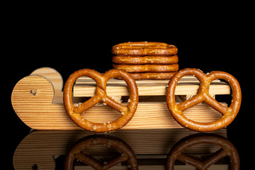 Group of six whole salty brown pretzel with wooden sledge isolated on black glass