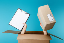 Hands Of Courier Holding Clipboard And Package From Cardboard Box Isolated On Blue