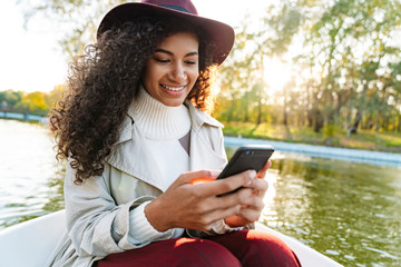 Cheerful young african woman wearing coat riding in a boat