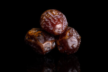 Group of three whole dry brown date fruit isolated on black glass