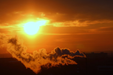 Wall Mural - red sun at sunset or dawn at dusk low above the horizon shrouded in smoke from the chimneys of the p