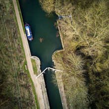 English Canal Scene With Barge, Lock And Towpath Surrounded By Winter Trees On A Bright February Day. Vertical Drone View.