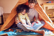 © Trevor Adeline/Caia Image - Father and daughter reading book in teepee