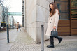 Side view of stylish brunette girl in coat dreamily walking around city street