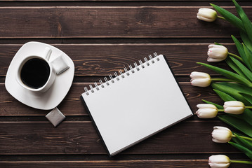 Wall Mural - White tulips on a wooden table with a Cup of coffee and an empty notebook