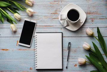 Wall Mural - Spring blanks of a freelancer's workplace with a bouquet of white tulips, a smartphone, an empty white bouquet and a Cup of coffee in his hands on wooden background