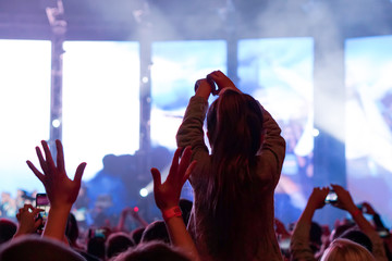 Child has fun on her parents' shoulders keeping hands with them at an outdoor rock music concert