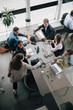 © Maskot - High angle view of businesswoman greeting colleagues at desk in creative office