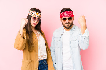 Wall Mural - Young caucasian couple wearing a music festival clothes isolated showing fist to camera, aggressive facial expression.