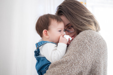 Wall Mural - Mother holding little infant baby on white background. Lifestyle family concept. 