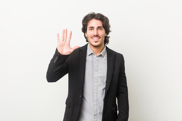 Young business man against a white background smiling cheerful showing number five with fingers.