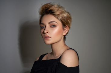 Portrait of young girl with blond fashionable hairstyle looking at camera isolated on gray background