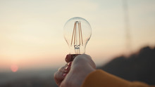 Close Up Hands Woman Holds A House Light Bulb At Sunset Renewable Energy Nature Electricity Innovation Green Invention Responsibility Environment Adult Power Protect Lamp Slow Motion