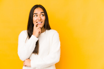 Wall Mural - Young woman isolated on a yellow background relaxed thinking about something looking at a copy space.