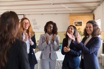 Smiling workers applauding colleague. Cheerful office managers standing and looking at coworker in office. Concept of success