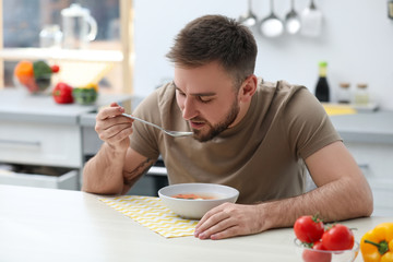 Poster - Young man eating tasty vegetable soup at table in kitchen