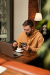 © New Africa - Male blogger with cup of coffee using phone at table in cafe