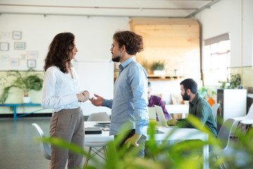 Wall Mural - Side view of serious man talking with confident colleague. Two coworkers communicating in open space office. Communication concept