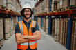 © StratfordProductions - Cheerful male worker entrepreneur in uniform with white hardhat and arms crossed standing in from of warehouse rack arrangement wearing spectacles